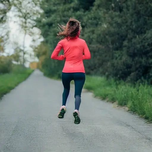 Woman jogging outdoors on paved path wearing pink jacket and dark leggings