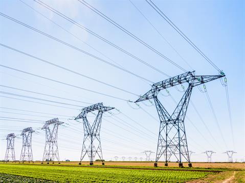 Row of electrical transmission towers stretching across green field under blue sky